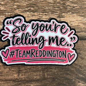 May include: A die-cut sticker featuring the black text "So you're telling me.." in a stylized script font, followed by a pink brushstroke background with the black text "#TEAMREDDINGTON" and two small pink hearts on the left and right sides.
