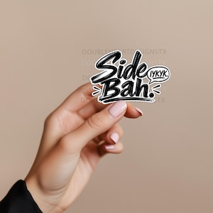 May include: A die-cut vinyl sticker featuring the black brush-lettered text Side Bah. with a smaller speech bubble containing the text IYKYK. The design has a white border and a black outline, presented against a solid light beige background.