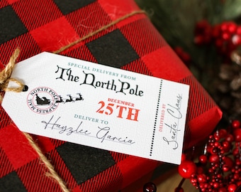 Może przedstawiać: Biała etykieta prezentowa z czarnym tekstem, który brzmi "SPECIAL DELIVERY FROM The North Pole DECEMBER 25TH DELIVER TO Hagzlee Garcia DELIVERED BY Santa Claus". Etykieta jest przywiązana sznurkiem do czerwono-czarnej pudełka prezentowej w kratę.
