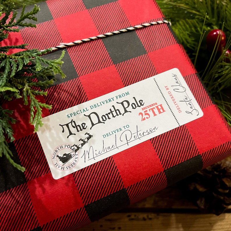 Może przedstawiać: Biała etykieta prezentowa z czarnym tekstem, kt&oacute;ry brzmi "SPECIAL DELIVERY FROM The North Pole DECEMBER 25TH DELIVER TO Michael Peterson DELIVERED BY Santa Claus". Etykieta znajduje się na czerwono-czarnym papierze do pakowania w kratkę.