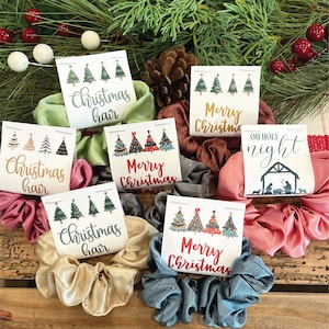 May include: Six Christmas-themed scrunchies with matching cards. The cards feature illustrations of Christmas trees and the text "Christmas hair", "Merry Christmas", and "Oh Holy Night".