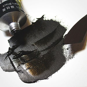 May include: A tube of black acrylic paint with the text "Mars Black 961 芳  墨" on the side. The paint is being squeezed out onto a white surface with a black palette knife.