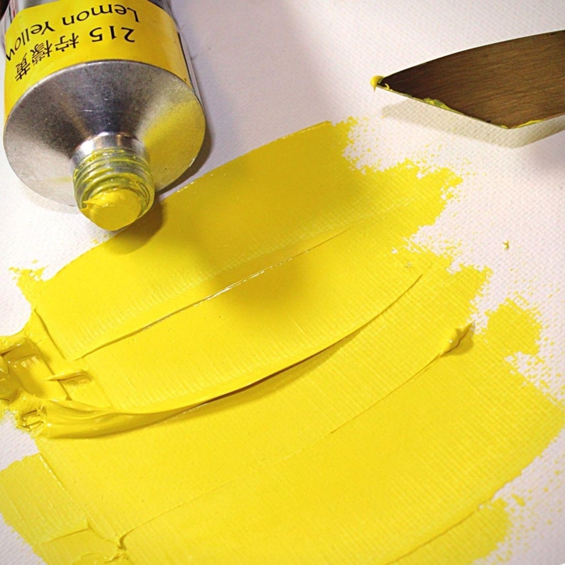 May include: A tube of lemon yellow paint with the text "215 Lemon Yellow" on the label. The paint has been squeezed out onto a white surface, creating a yellow stripe.