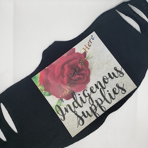 Puede incluir: Máscara facial negra con una rosa roja y el texto "You are here" e "Indigenous Supplies" impreso en ella.