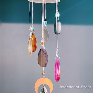 May include: A crystal and agate mobile with a crescent moon design. The mobile features iridescent crystals, agate slices in various colors, and a clear crystal drop. The mobile is labeled "Iridescent Frost".