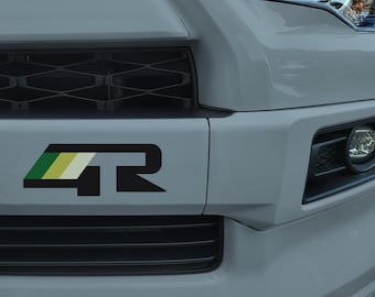 Può includere: Un'auto grigia con una griglia nera e un adesivo "4R" nero e verde sul paraurti anteriore.