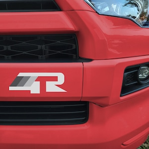 May include: A red car with a black grille and a white "4R" emblem on the front bumper.