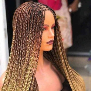 May include: A long, straight, braided wig with a two-toned ombre color scheme. The wig is a mix of dark brown and light blonde, with the lighter color starting at the bottom and fading into the darker color. The wig is styled in a straight, sleek style, with the braids hanging down the back of the head.