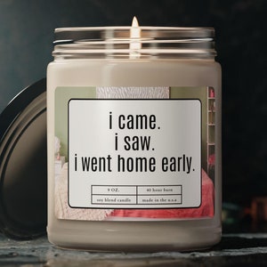Könnte beinhalten: Eine Sojawachskerze in einem Glasgefäß mit einem Etikett, auf dem "i came. i saw. i went home early." steht. Die Kerze ist angezündet und die Flamme ist sichtbar.