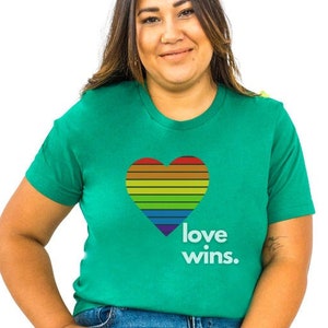 Puede incluir: Una persona con una camiseta verde con un corazón arcoíris y el texto "love wins."