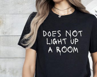 Op de afbeelding: Zwart T-shirt met witte tekst die "DOES NOT LIGHT UP A ROOM" zegt.