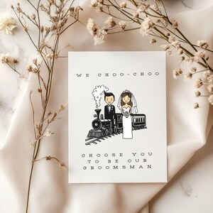 May include: A white card with a black illustration of a bride and groom standing in front of a train. The text on the card reads "WE CHOO-CHOO CHOOSE YOU TO BE OUR GROOMSMAN."