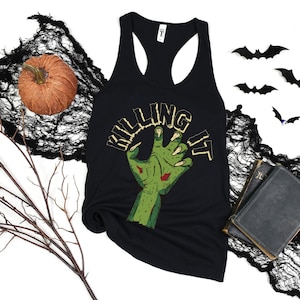 Puede incluir: Camiseta negra de tirantes con un gráfico de mano de zombie verde y el texto "KILLING IT".