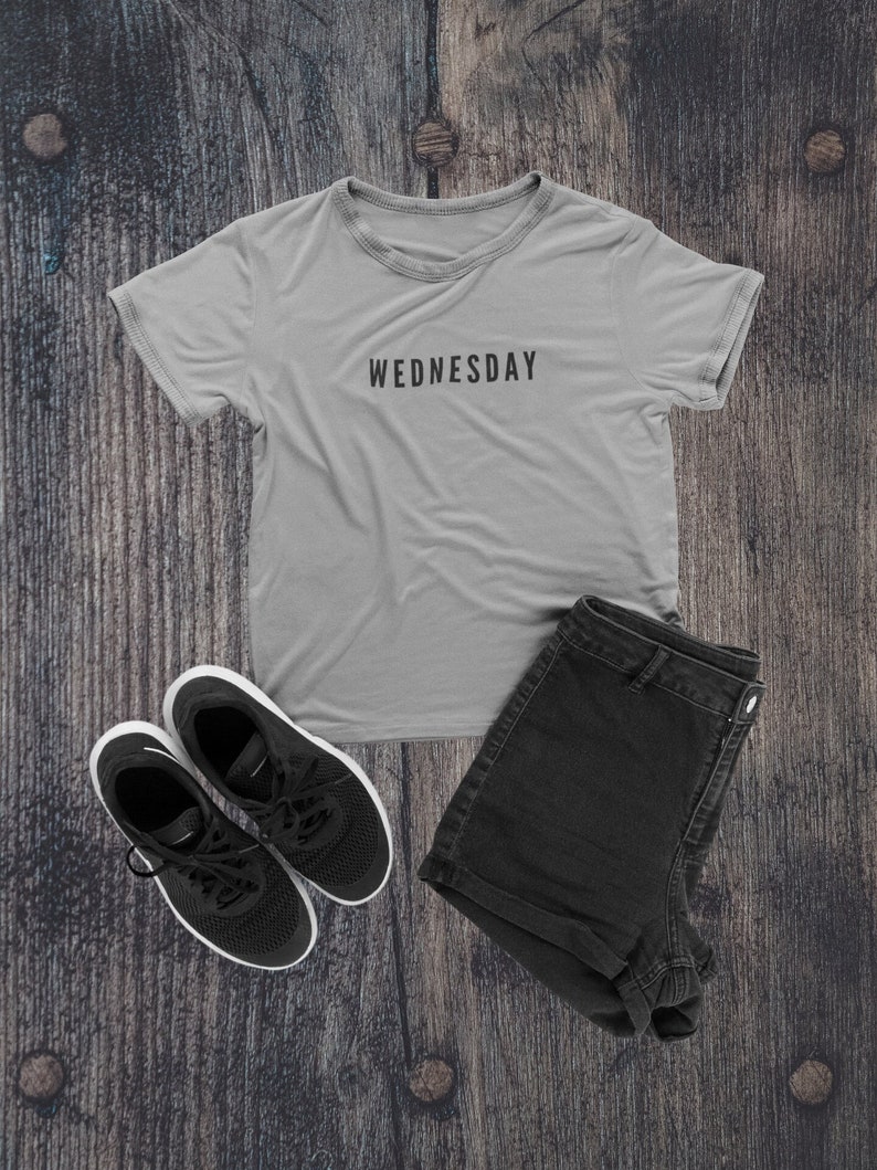 Peut inclure: Un t-shirt gris avec le mot "WEDNESDAY" imprim&eacute; sur le devant, un short en jean noir et une paire de baskets noires.