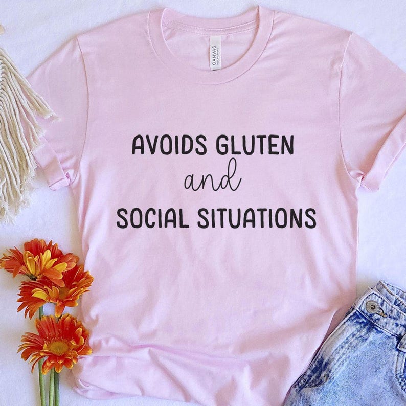 May include: Pink t-shirt with the text "Avoids Gluten and Social Situations" printed in black.