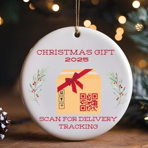 May include: White ceramic Christmas ornament with gold string. The ornament features the text "CHRISTMAS GIFT 2025" and "SCAN FOR DELIVERY TRACKING" in red. A graphic of a gift box with a red bow and a QR code is in the center, with sprigs of greenery on either side.