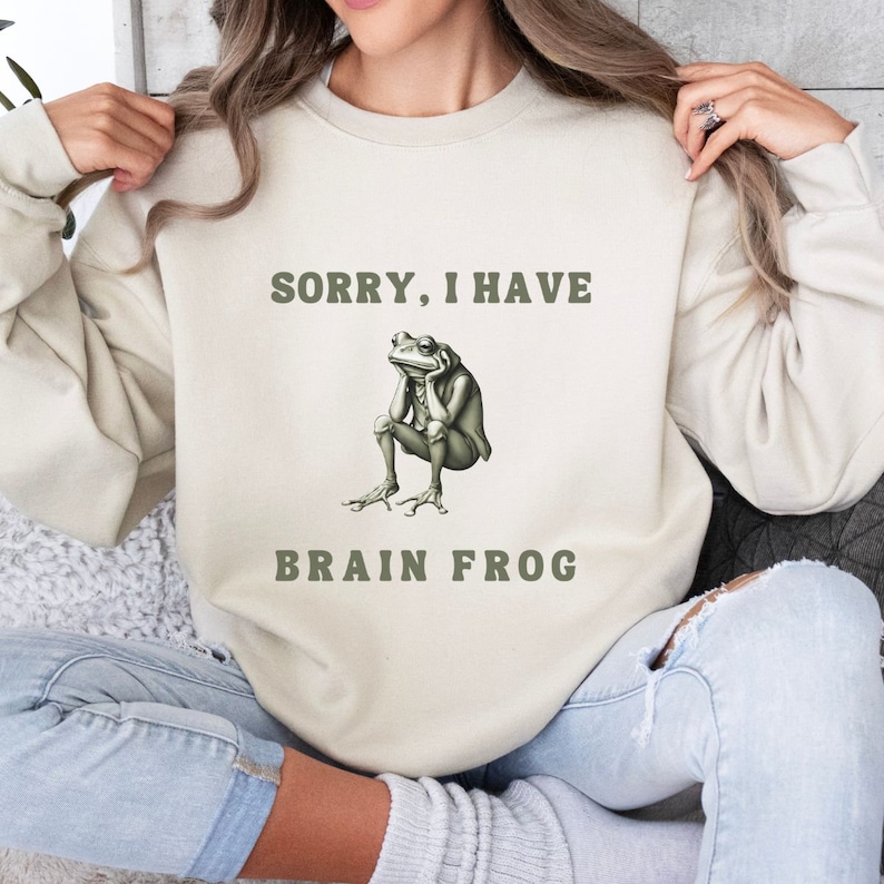 May include: A beige sweatshirt with the text "Sorry, I have Brain Frog" and a cartoon frog with a thinking expression.
