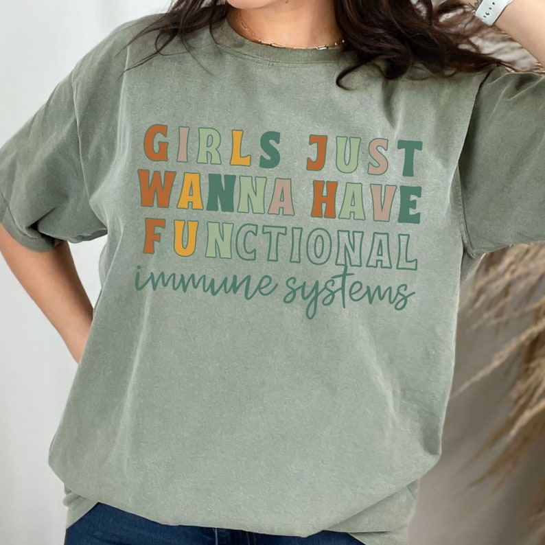 May include: A green t-shirt with the text "Girls Just Wanna Have Functional Immune Systems" in colorful letters.
