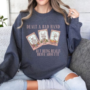 May include: A navy blue sweatshirt with the text "Dealt a bad hand but being really brave about it" and three tarot cards with the words "Cog Fog", "Fatigue", and "Chronic Pain".