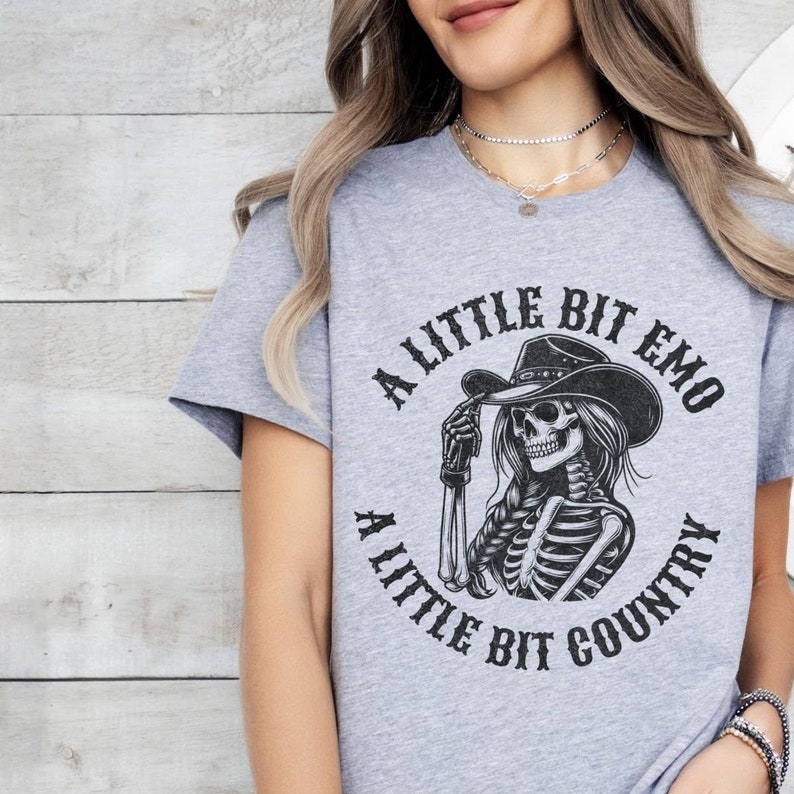 May include: Gray t-shirt with a black and white graphic of a skeleton wearing a cowboy hat. The text on the shirt reads "A little bit emo a little bit country".