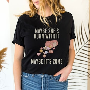 May include: Black t-shirt with the text "Maybe she's born with it, maybe it's 20mg" and a graphic of a pill bottle spilling out pills with smiley faces and flowers.