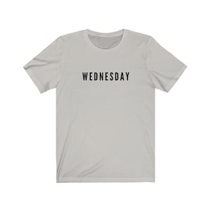 Peut inclure: Un t-shirt gris clair avec le mot "WEDNESDAY" imprim&eacute; en noir sur le devant.