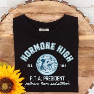 May include: Black t-shirt with a blue and white graphic design that says "Hormone High" with a possum illustration and the text "EST. 1882" and "P.T.A. President patience, tears and attitude".