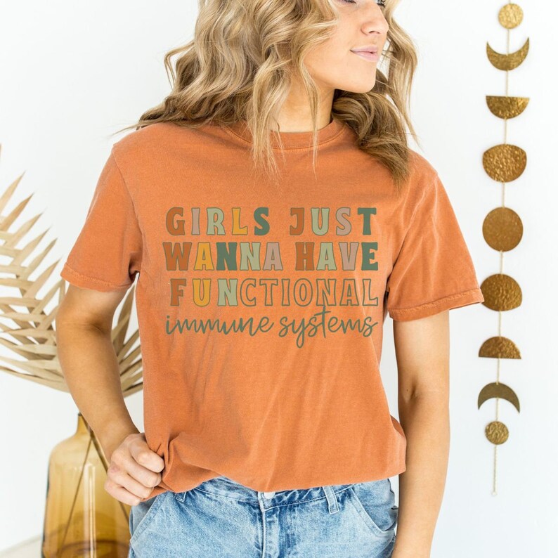 May include: A burnt orange t-shirt with the text "Girls Just Wanna Have Functional Immune Systems" in a rainbow of colors.