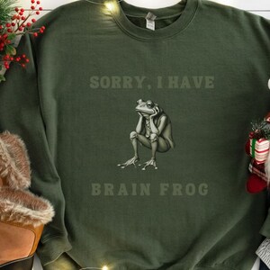 May include: A green sweatshirt with the text "Sorry, I have Brain Frog" and a cartoon frog with a thoughtful expression.