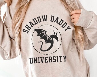 May include: A beige sweatshirt with a black graphic of a dragon in a circle with the text "Shadow Daddy University" around it.