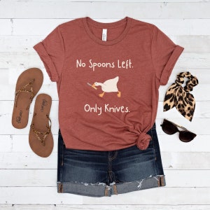 May include: A rust-coloured t-shirt with the text "No Spoons Left. Only Knives." and a cartoon image of a goose holding a knife.