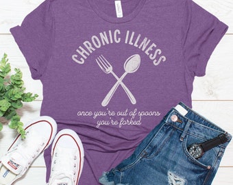 May include: Purple t-shirt with the text "CHRONIC ILLNESS" and a white fork and spoon crossed over each other. Below the text is the phrase "once you're out of spoons you're forked".