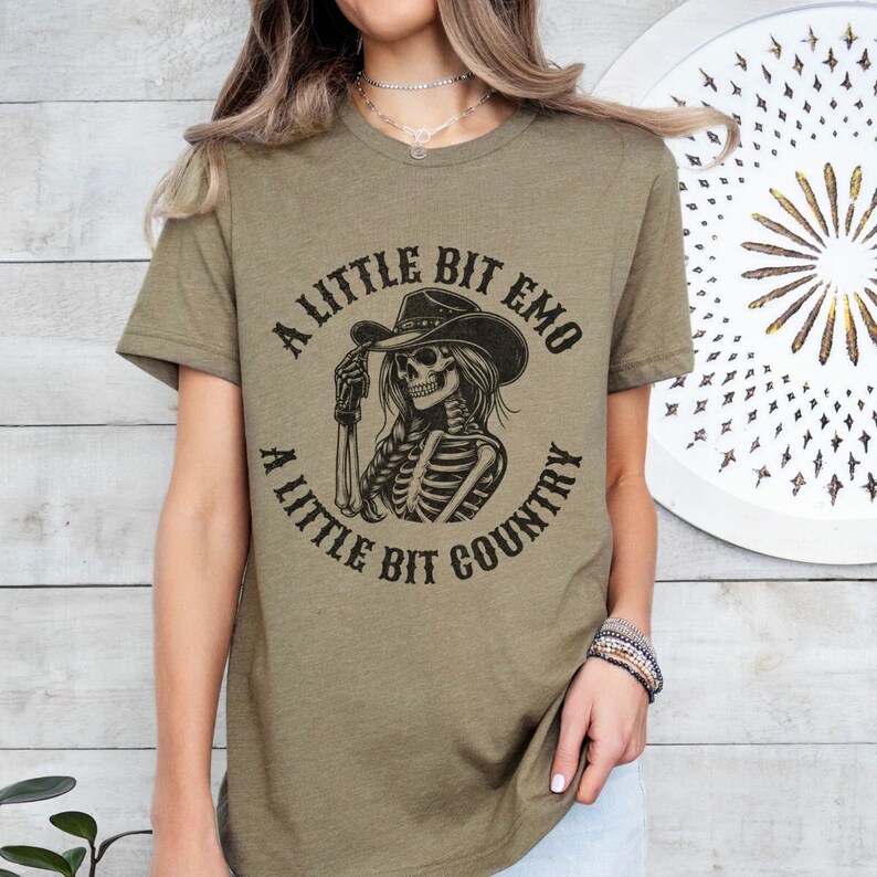 May include: A green t-shirt with a black and white graphic of a skeleton wearing a cowboy hat. The graphic has the text "A Little Bit Emo A Little Bit Country".