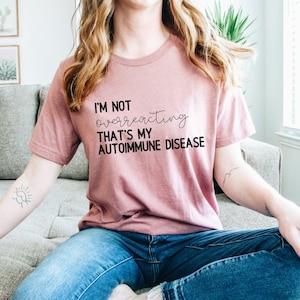 May include: A pink t-shirt with the text "I'm not overreacting that's my autoimmune disease" printed in black.