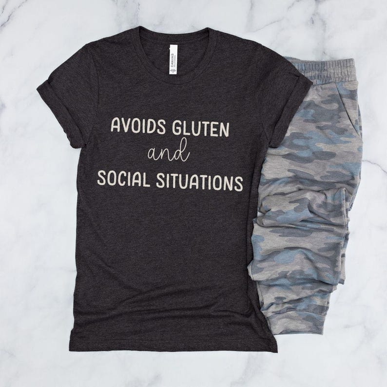 May include: A dark grey t-shirt with the text "Avoids Gluten and Social Situations" printed in white.