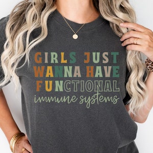 May include: A dark gray t-shirt with the text "Girls Just Wanna Have Functional Immune Systems" in colorful, retro-style lettering.