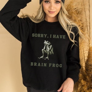 May include: Black sweatshirt with a green frog graphic and the text "Sorry, I have brain frog".