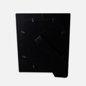 K&ouml;nnte beinhalten: Eine rechteckige schwarze Bilderrahmenr&uuml;ckwand mit einer samtartigen schwarzen Oberfl&auml;che. Die R&uuml;ckseite verf&uuml;gt &uuml;ber einen klappbaren Aufsteller f&uuml;r die Tischpr&auml;sentation, einen Metallhaken zur Wandmontage und mehrere drehbare Metallclips.