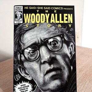 May include: A black and white comic book cover featuring a close-up portrait of Woody Allen. The cover text reads "He Said/She Said Comics Presents The Woody Allen Story".