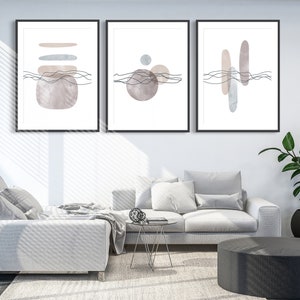 Puede incluir: Tres impresiones de arte abstracto enmarcadas con un diseño minimalista que presenta formas de acuarela en tonos de gris, marrón y beige. Las impresiones están colgadas en una pared blanca sobre un sofá blanco.