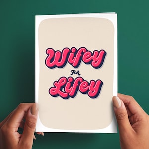 May include: A rectangular greeting card with a cream-colored background featuring the text Wifey For Lifey in a bold, pink, bubble-style font with a dark blue shadow effect. The card has rounded corners and is presented against a dark green background.
