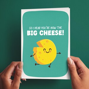 May include: A greeting card with a teal background featuring a yellow cartoon cheese wheel with a smiling face, arms, and legs. The text at the top reads, "SO I HEAR YOU'RE NOW THE BIG CHEESE!" in white, bold, sans-serif capital letters.
