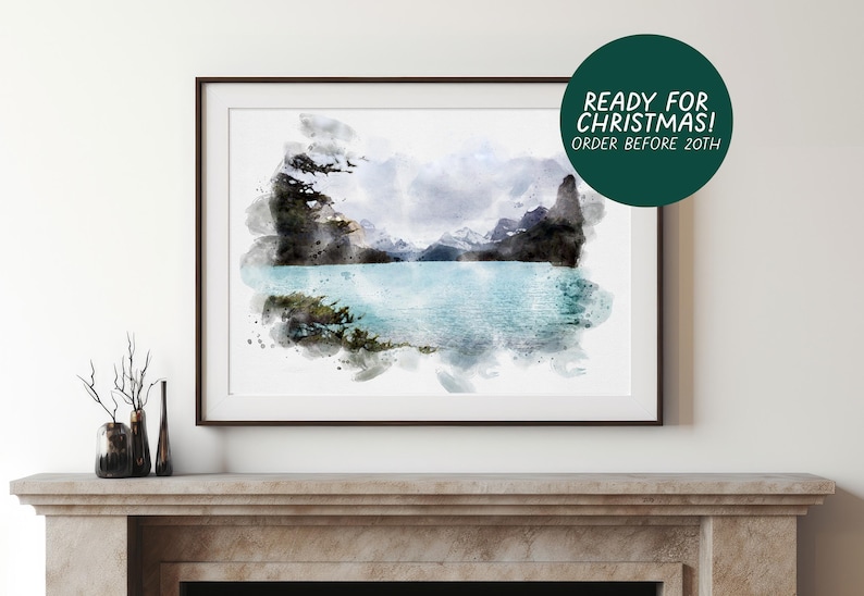 May include: A framed watercolor landscape print depicting a turquoise glacial lake surrounded by dark, jagged mountain peaks and evergreen trees. The artwork features a soft, blended aesthetic with visible paint strokes and a white border.
