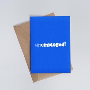 以下が含まれることがあります： 白い文字で「unemployed!」と書かれた青いカード。カードは茶色の封筒の上に置かれている。