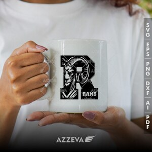 May include: A white ceramic mug with a black and white graphic of a ram's head inside the letter "R" and the word "RAMS" below. The mug is being held by a person's hands.