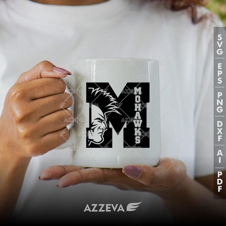 May include: White ceramic mug with a black and white graphic of a stylized letter M with a Mohawk warrior's head inside the letter. The text "MOHAWKS" is vertical along the right side of the letter M.
