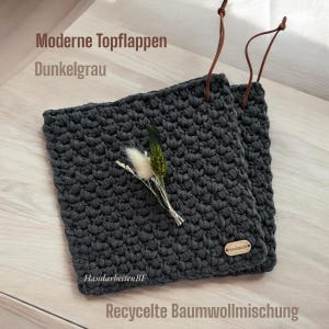 Könnte beinhalten: Zwei dunkelgraue gehäkelte Topflappen mit Lederösen. Die Topflappen sind aus recycelter Baumwollmischung gefertigt. Der Text "Moderne Topflappen Dunkelgrau" und "HandarbeitenBF" ist auf den Topflappen sichtbar.