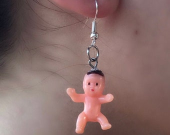 Op de afbeelding: Een paar zilveren oorhangers met een kleine roze plastic babypopbedel.