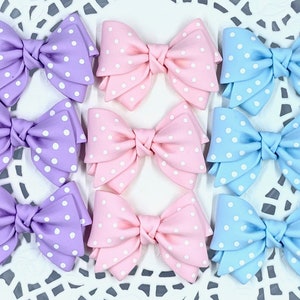 May include: Nine handmade fabric bows with white polka dots. Three bows are lavender, three are pink, and three are light blue.