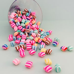 May include: A glass bowl filled with colorful candy, spilling out onto a light blue surface. The candy is in the shape of small squares with stripes of pink, blue, green, yellow, and brown.